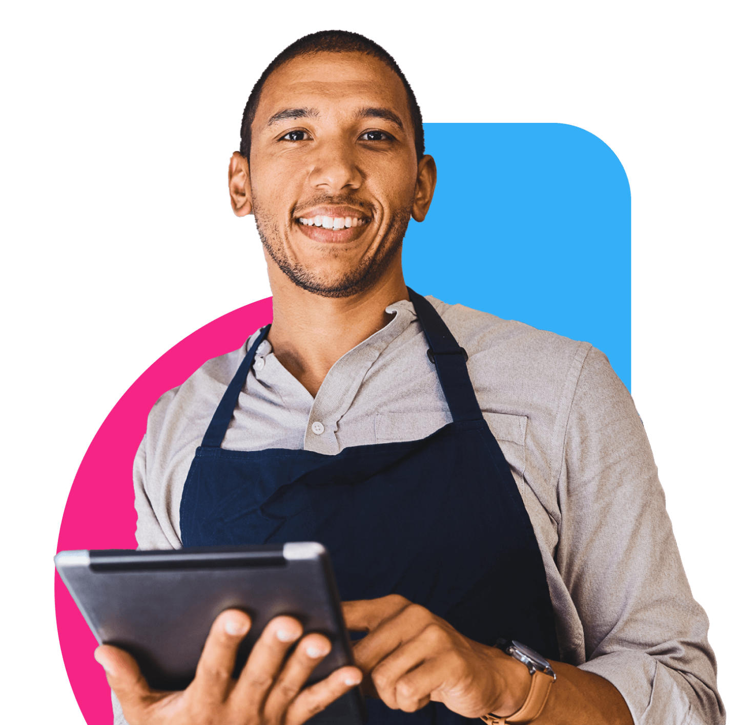 A young black man holding a tablet smiling at the camera, wearing a button down shirt and an apron