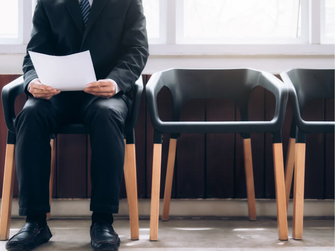 Male applicant for a job is waiting in a waiting room wearing a suit and holding his resume